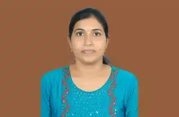 Portrait of a woman with dark hair tied back, wearing a turquoise kurta with pink embroidery, against a brown background.